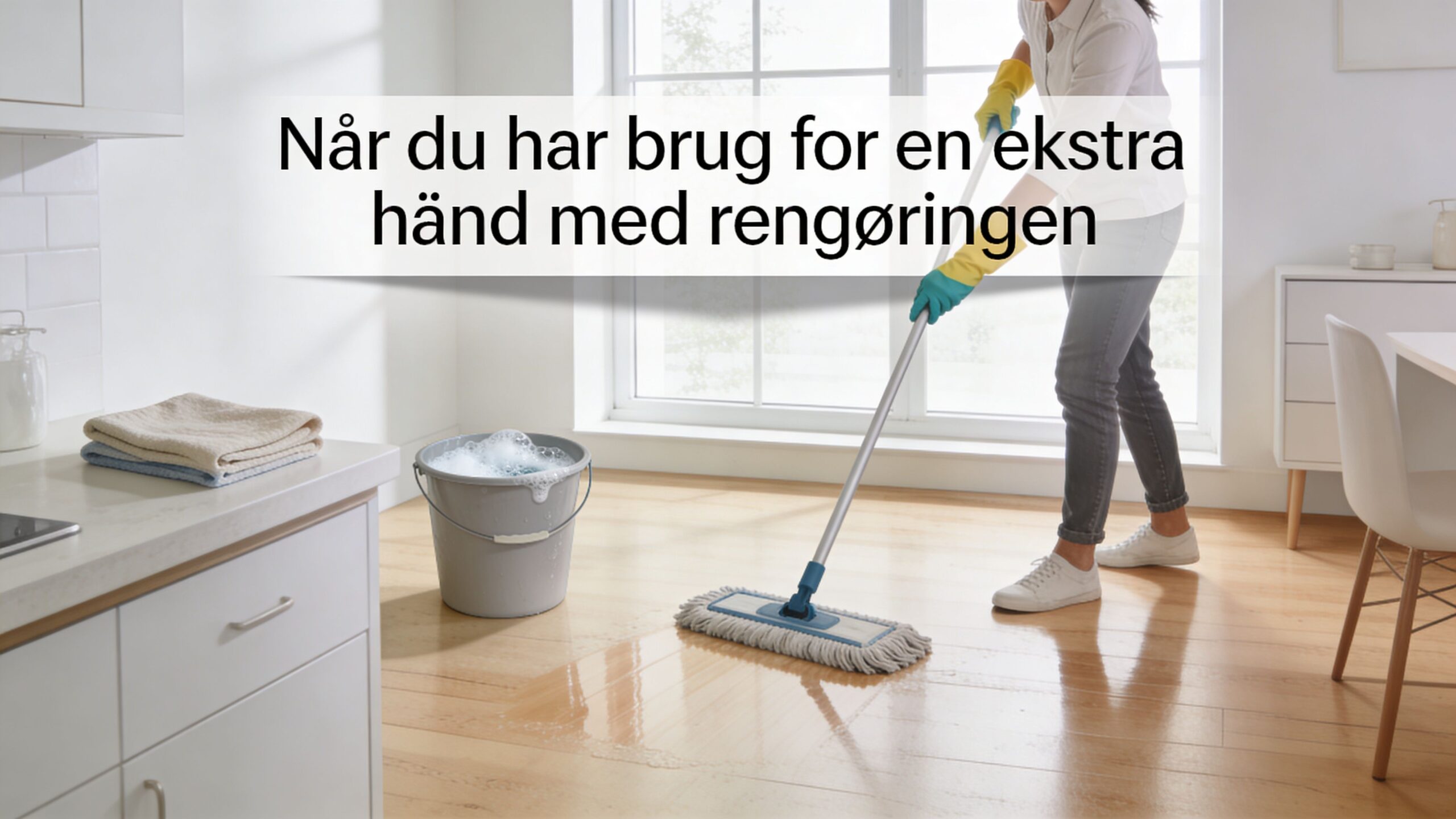 En person vasker et trægulv med en moppe og en spand med sæbevand i et lyst køkken.