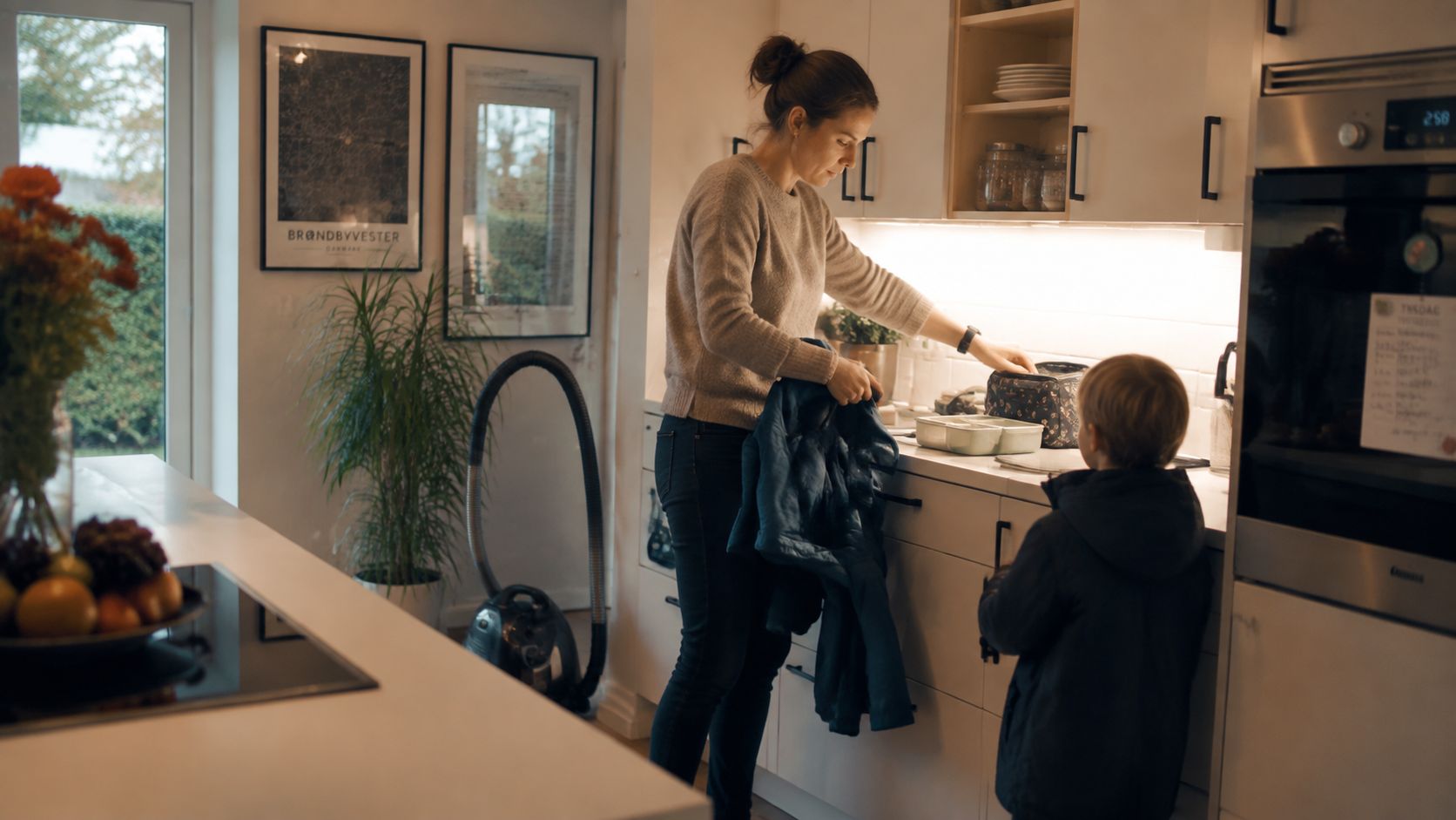 En mor gør en madpakke klar til sit barn i køkkenet i et moderne lyst hjem.